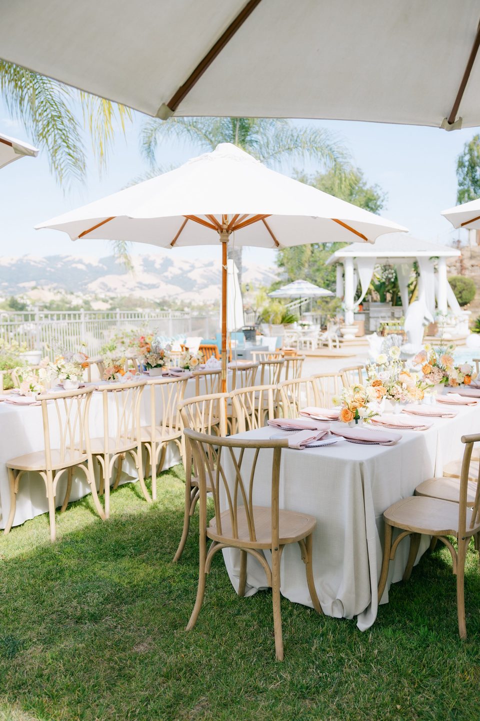 Outdoor event tablescape with white umbrellas, floral arrangements, and mountain views by Lovely Moments Planning